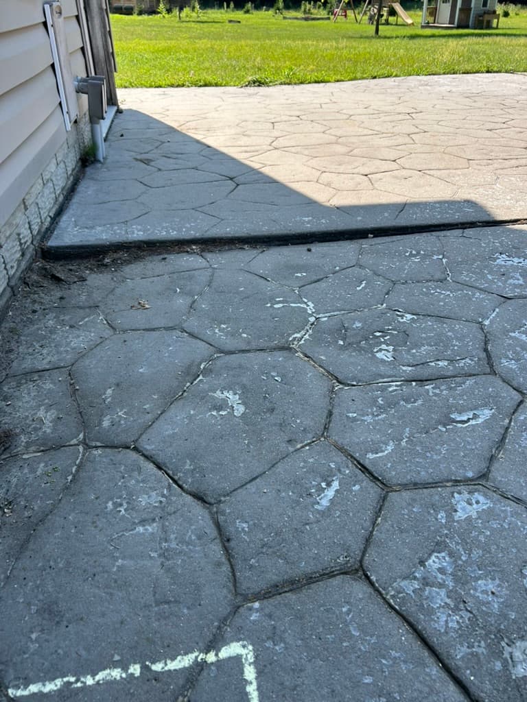 A settled stamped-concrete patio dropped low at the house, with a lip at the transition