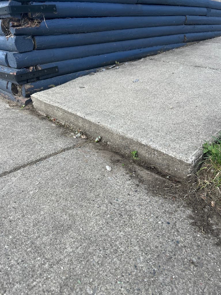 A sidewalk slab raised into a trip-hazard lip beside a landscaped bed
